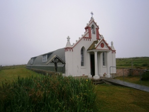 The Chapel exterior. The wayside shrine to the left is centred on a gift made in 1961 of Christ crucified  from Domenica Chiocchetti's home town of Moena to the people of Orkney with the cross and canopy made in Kirkwall.